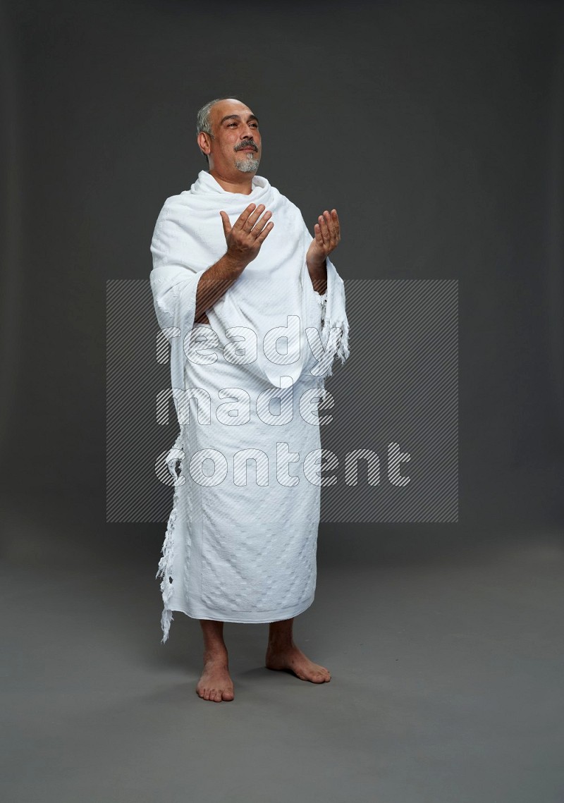 A man wearing Ehram Standing dua'a on gray background