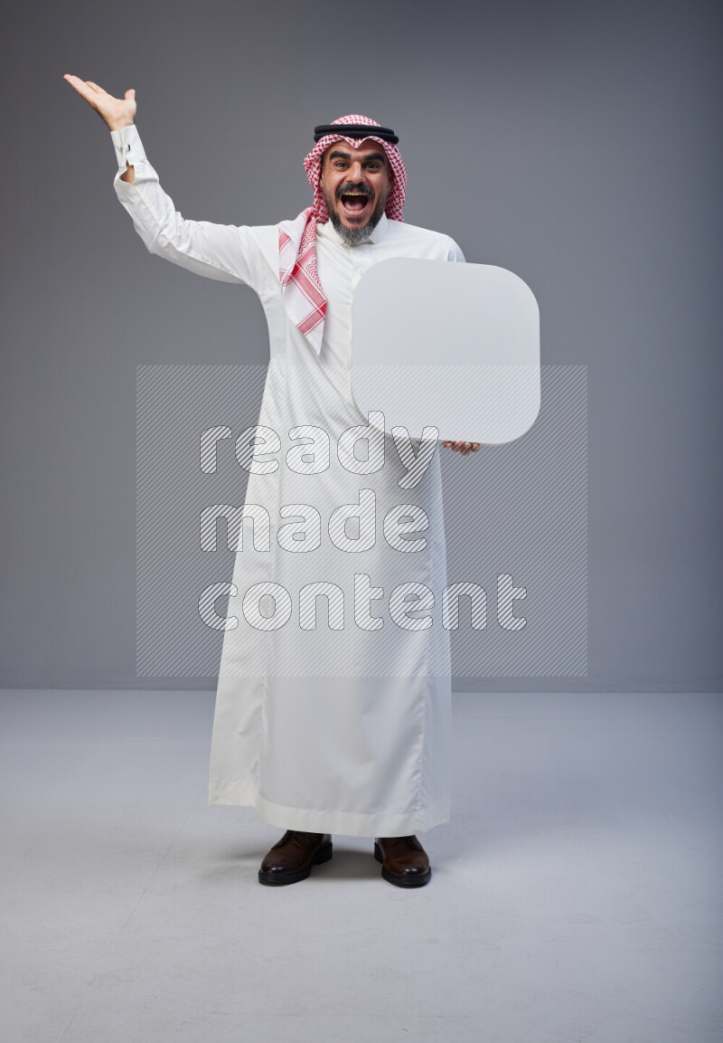 Saudi man Wearing Thob and red Shomag standing holding social media sign on Gray background