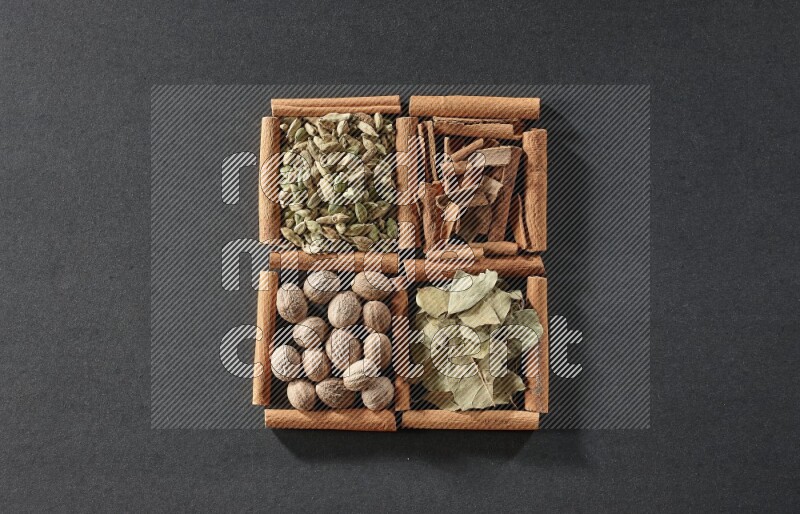 4 squares of cinnamon sticks full of cinnamon, cardamom, bay laurel leaves and nutmegs on black flooring