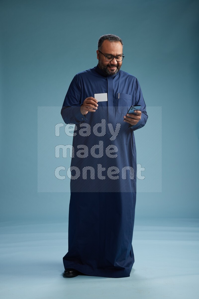 Saudi Man without shimag Standing holding ATM while talking on phone on blue background