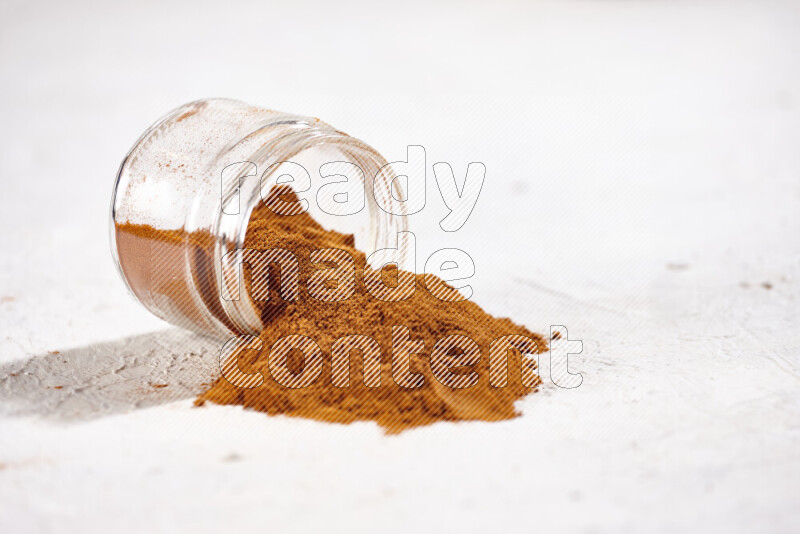 A glass jar full of ground paprika powder flipped with some spilling powder on white background