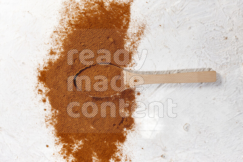 A wooden spoon full of ground paprika powder and surrounded with the powder on white background