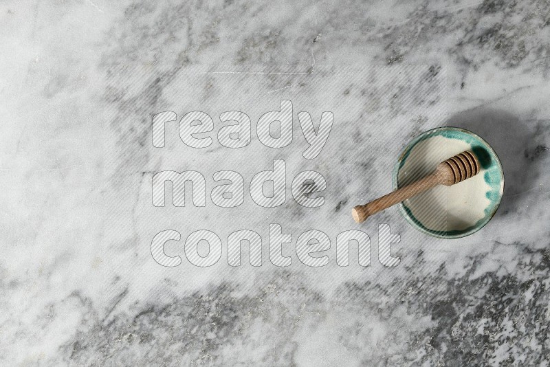 Multicolored Pottery Bowl with wooden honey handle in it, on grey marble flooring, Top View