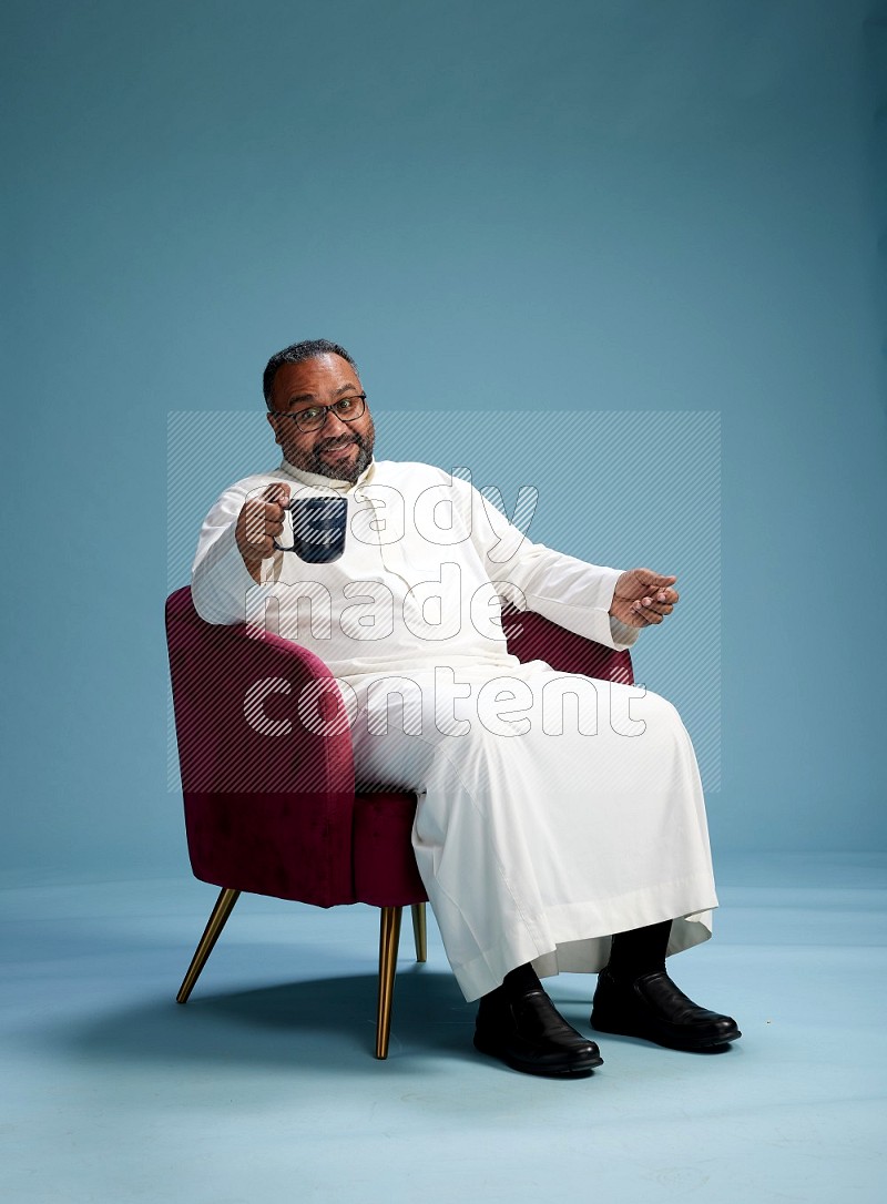 Saudi Man without shimag sitting on chair drinking coffee on blue background