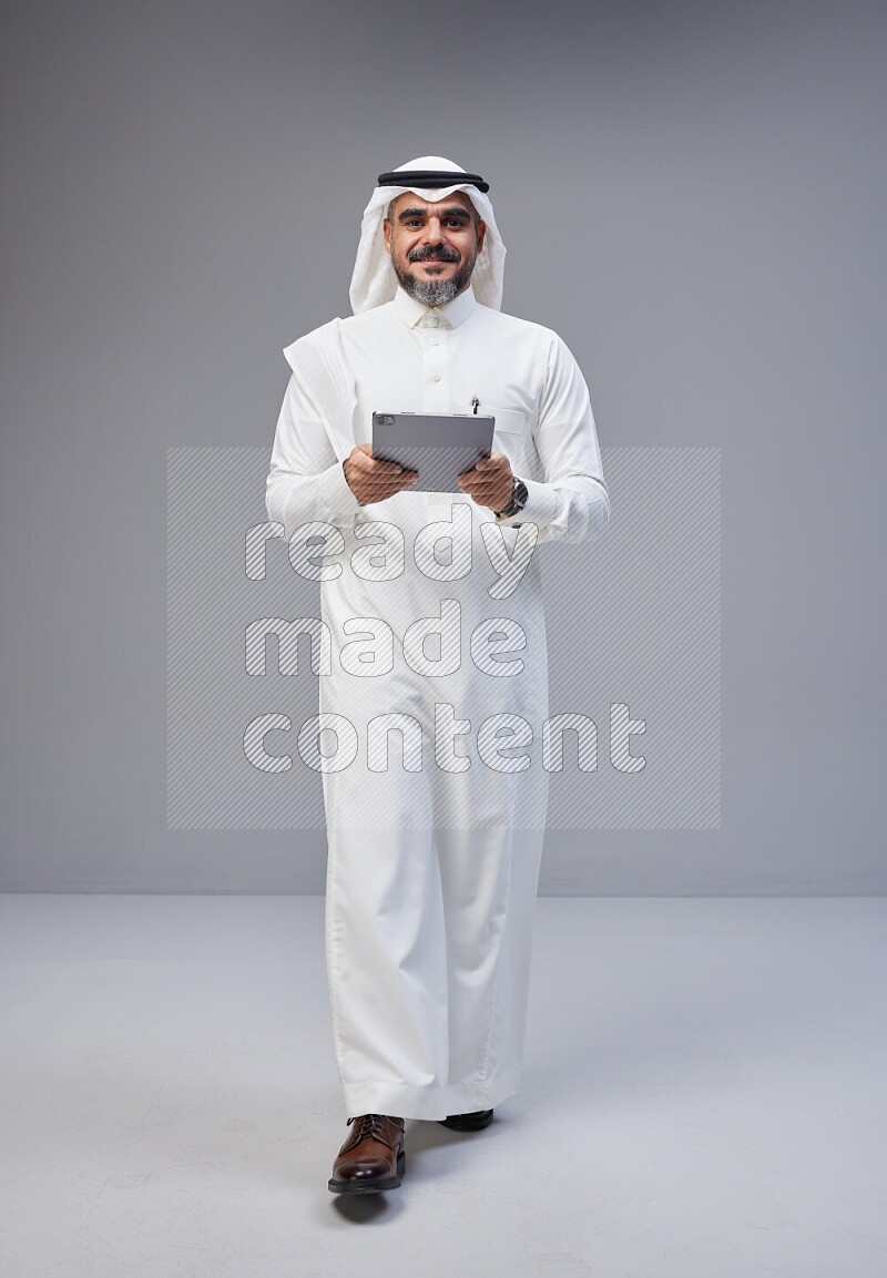 رجل سعودي يرتدي ثوب وشماغ ابيض يحمل تابلت ويتفاعل امام الكاميرا