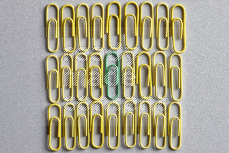 A bunch of yellow paper clips with a different colored paper clip in the center on grey background