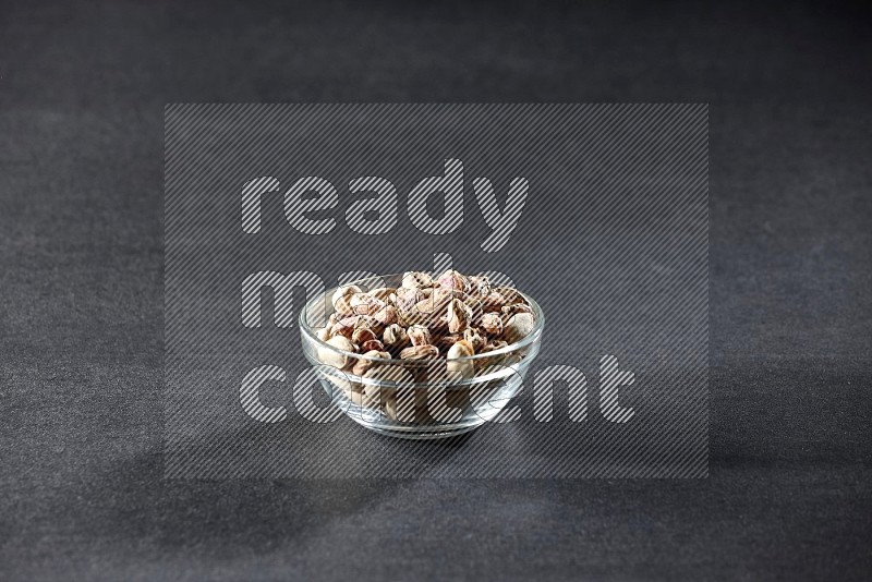A glass bowl full of peeled pistachios on a black background in different angles