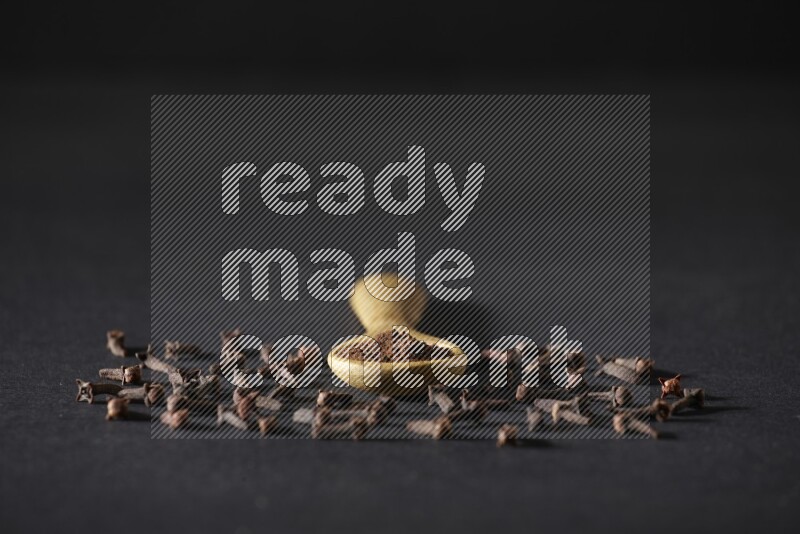 ملعقة خشبية ممتلئة ببودرة القرنفل مع حبوب القرنفل المتناثرة على خلفية سوداء