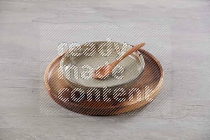 multi color pottery round dish on top of brown wood round plate and spoon, on grey textured countertop