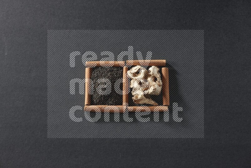 مربعان من أعواد القرفة ممتلئان بالزنجبيل المجفف والشاي الأسود علي خلفية سوداء