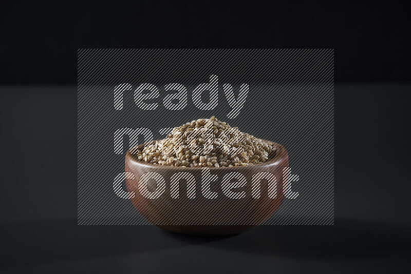 Hulled wheat in a wooden bowl on grey background