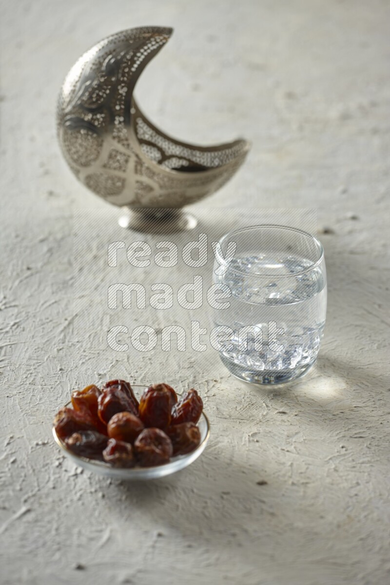 A silver lantern with different drinks, dates, nuts, prayer beads and quran on textured white background