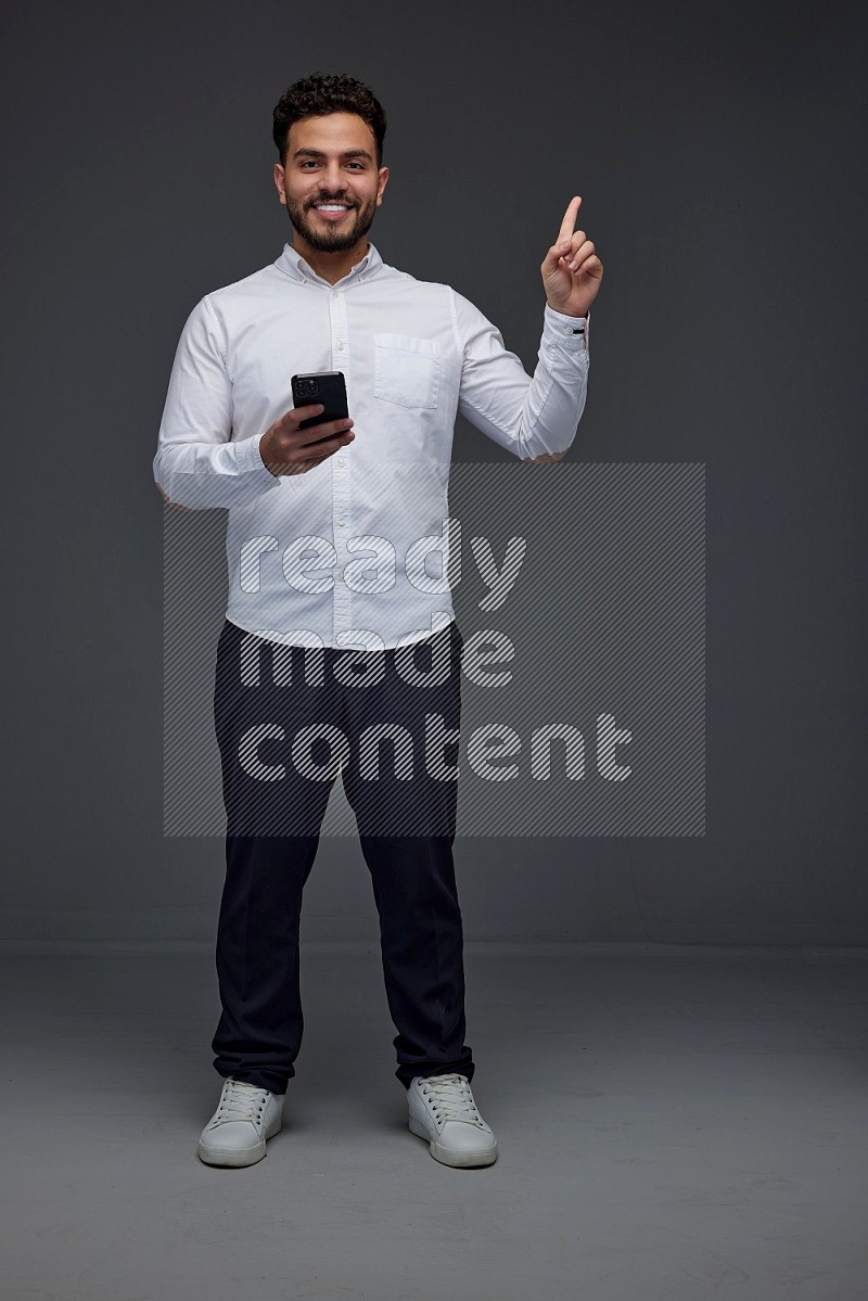 A man wearing smart casual standing and using his phone and making multi hand gestures eye level on a gray background