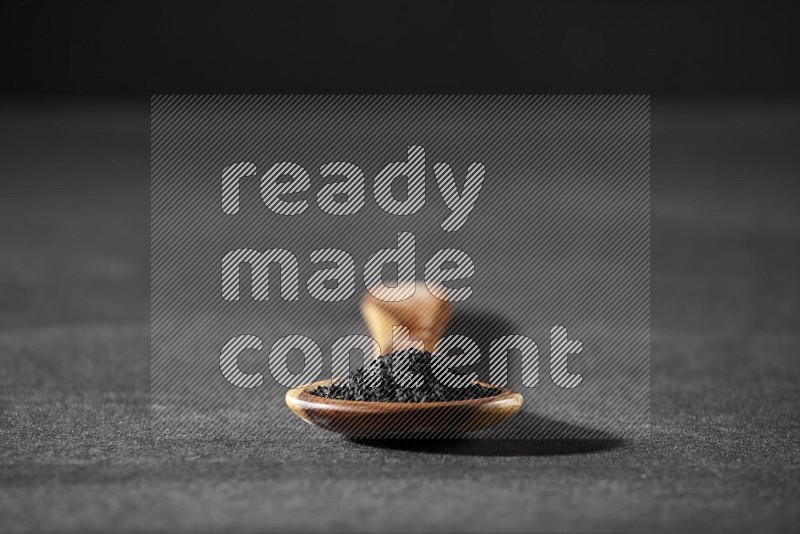 A wooden ladle full of black seeds on a black flooring