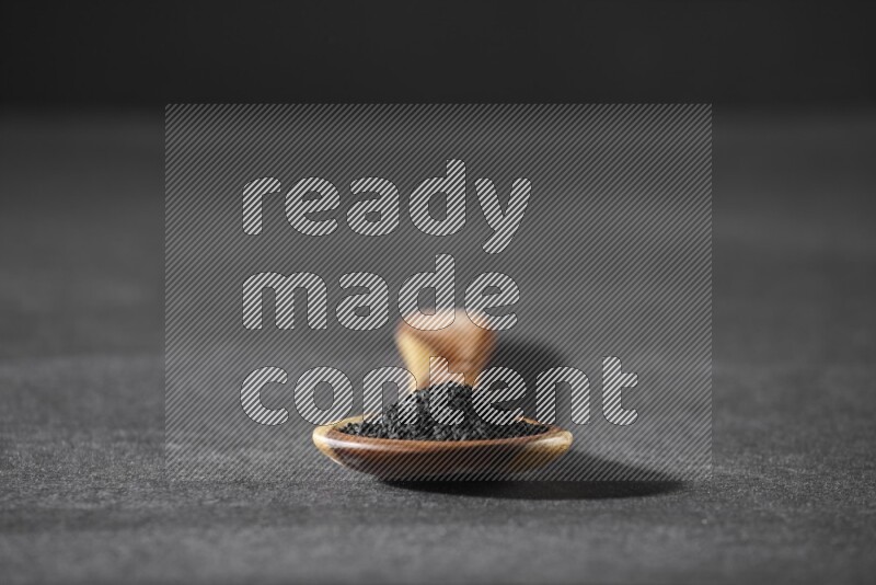 A wooden ladle full of black seeds on a black flooring