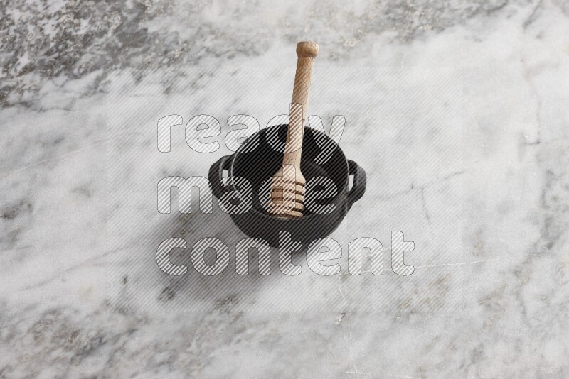 Black pottery bowl with wooden honey dipper in it on grey marble background