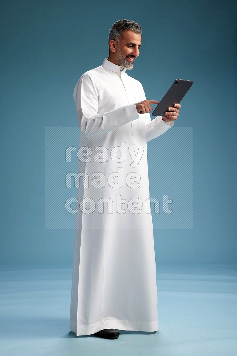 Saudi man waring thob with tablet on blue background