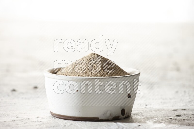 white pottery bowl full of white pepper powder on textured white flooring