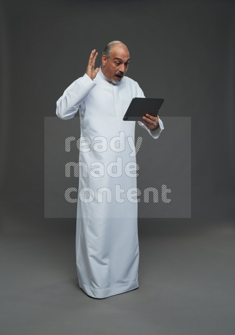 Saudi man without shomag Standing working on tablet on gray background
