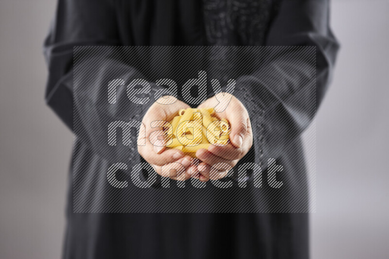 Woman in abaya holding different kinds of pasta in different positions
