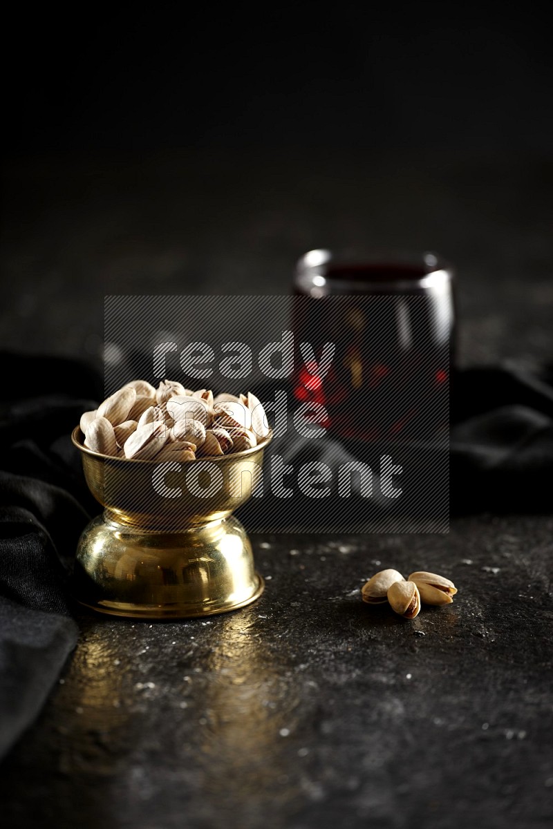 Nuts in a metal bowl with hibiscus and a napkin in a dark setup
