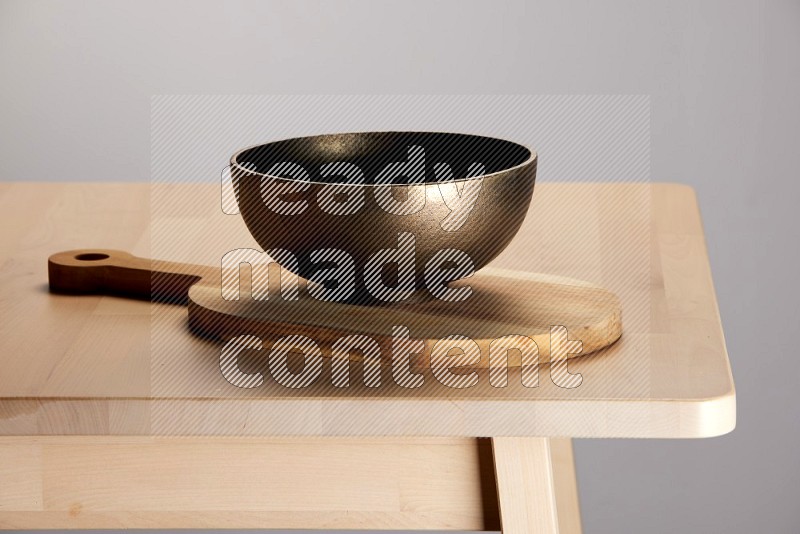 brass bowl placed on a  wooden oval cutting board on the edge of wooden table
