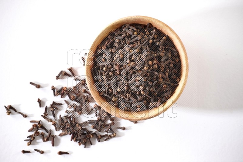 A wooden bowl full of cloves with spread grains on a white flooring