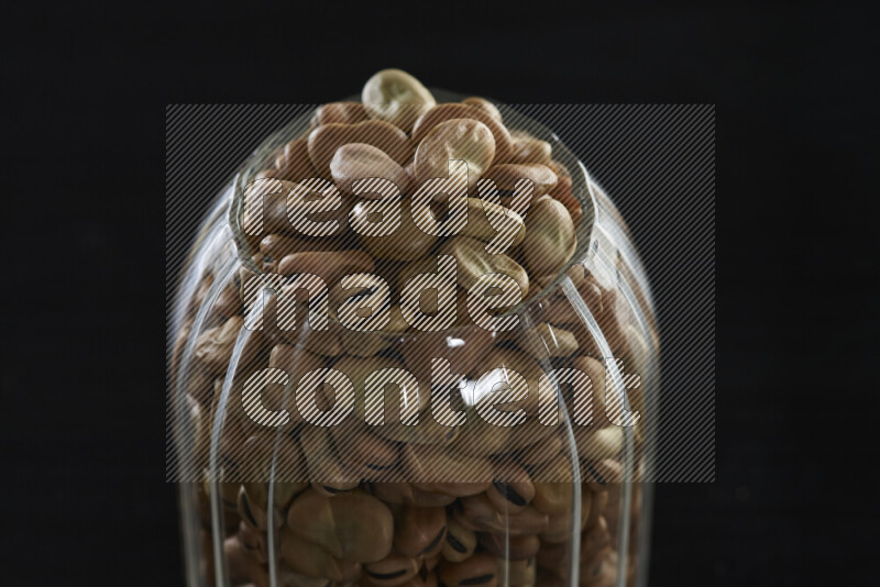 Fava beans in a glass jar on black background