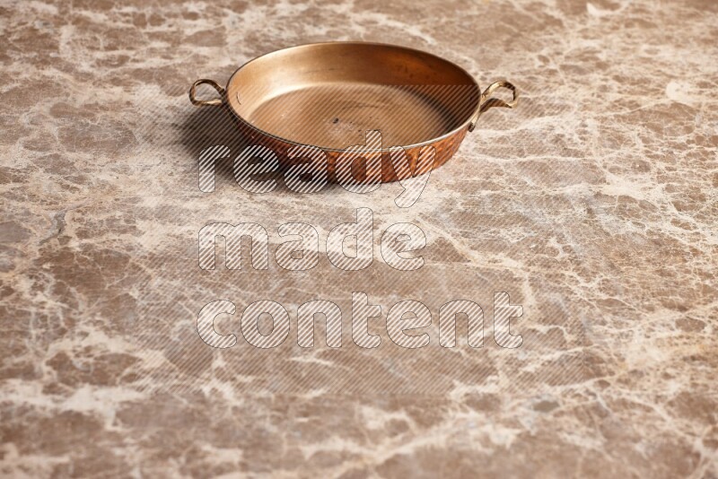 A small copper pan on beige marble background
