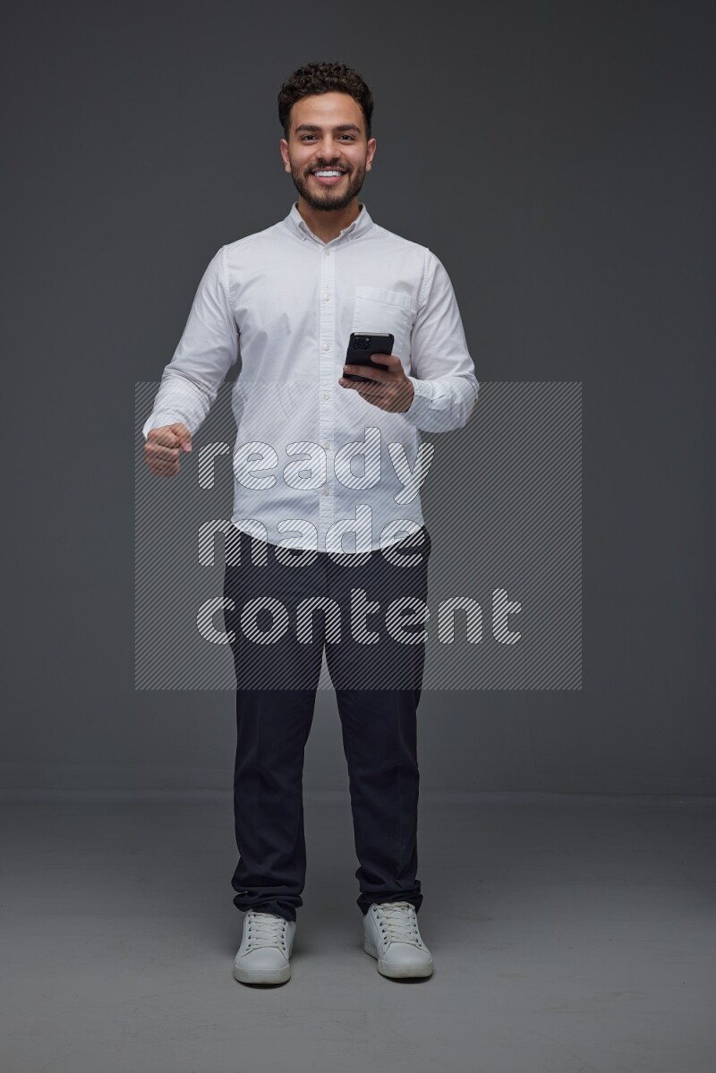 A man wearing smart casual standing and using his phone eye level on a gray background