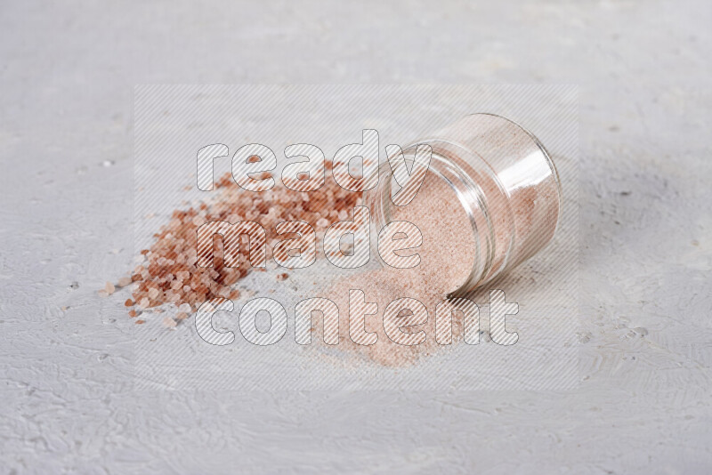 A glass jar full of fine himalayan salt with some himalayan crystals beside it on a white background