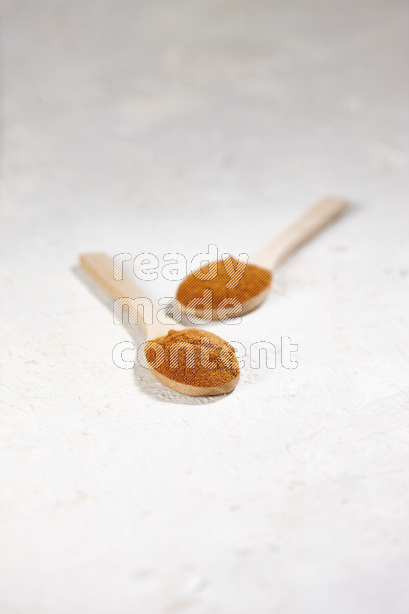 Two wooden spoons full of ground paprika powder on white background