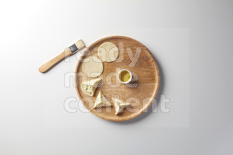 two closed sambosas and one open sambosa filled with cheese while oil with oil brush aside in a wooden dish on a white background