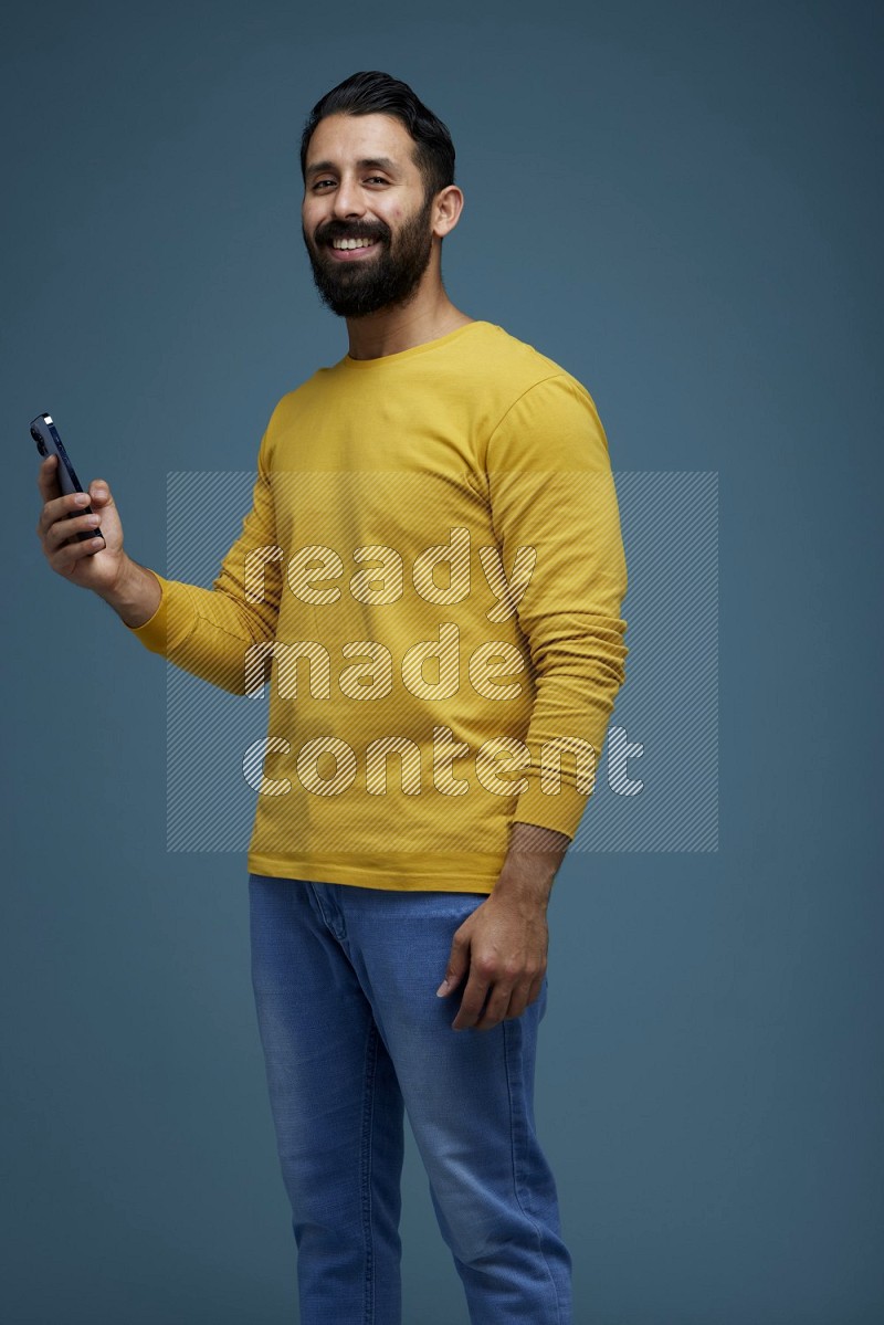 Man posing with a phone in a blue background wearing a yellow shirt