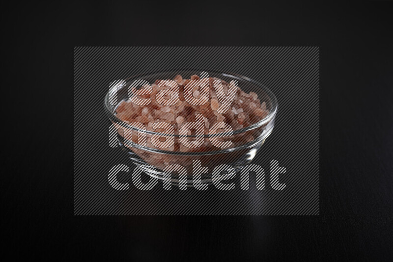 A glass bowl full of coarse himalayan salt crystals on black background