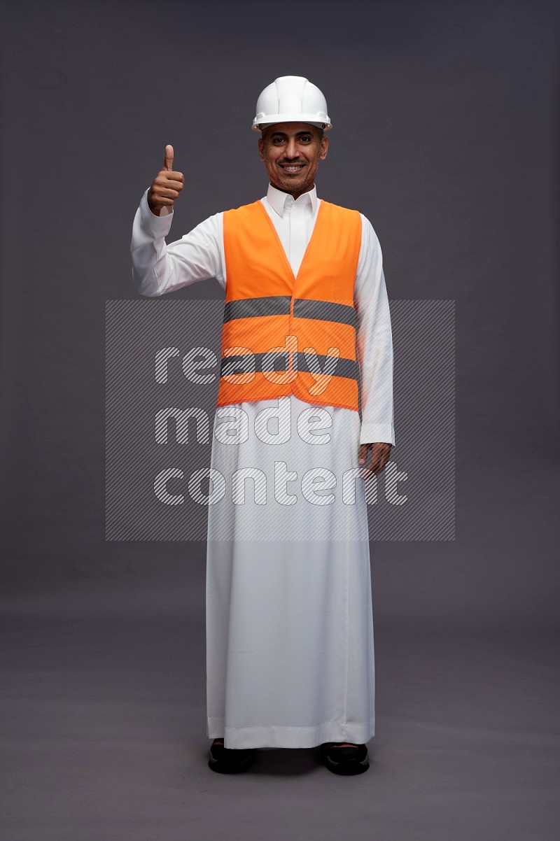 Saudi man wearing thob with engineer vest standing interacting with the camera on gray background