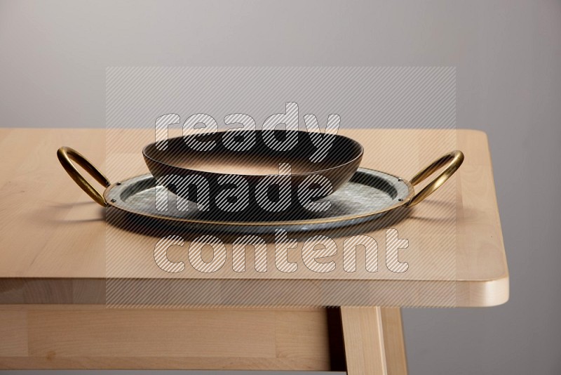 brass plate placed on a rounded stainless steel tray with golden handels on the edge of wooden table