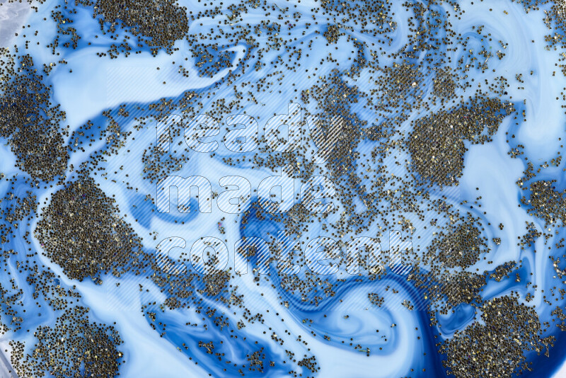 A close-up of sparkling gold glitter scattered on swirling blue background