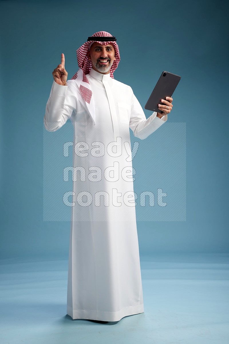 Saudi man wearing thob and shomagh with tablet on Blue background