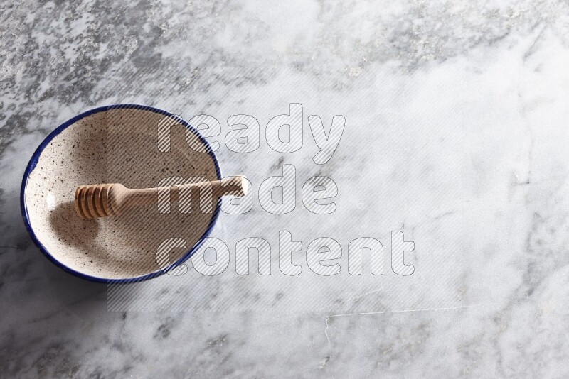 وعاء فخاري متعدد الألوان مع ملعقة عسل خشبية بداخله على خلفية من الرخام الرمادي