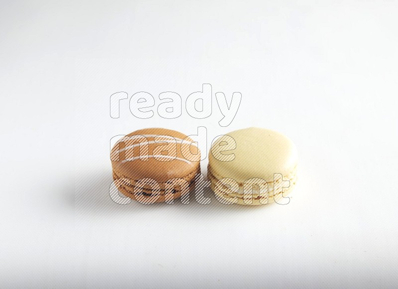 45º Shot of of two assorted Brown Irish Cream, and Yellow Vanilla macarons on white background