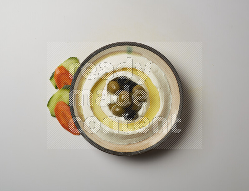 Lebnah garnished with whole black olives in a pottery plate on a white background