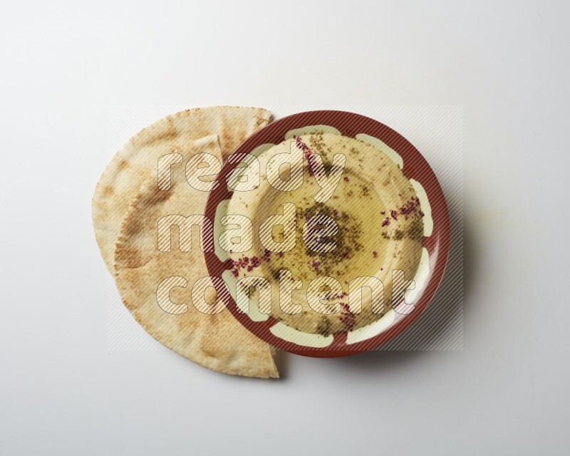 Hummus in a traditional plate garnished with zaatar & sumak on a white background