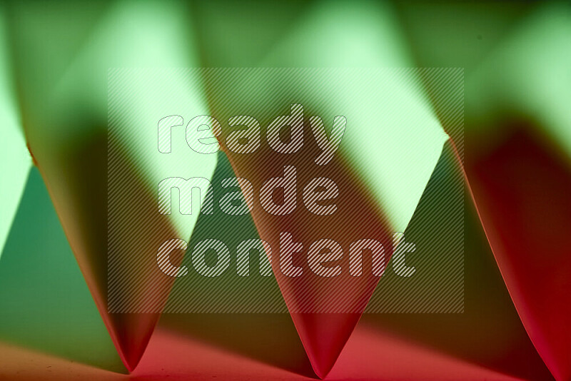 A close-up abstract image showing sharp geometric paper folds in green and red gradients