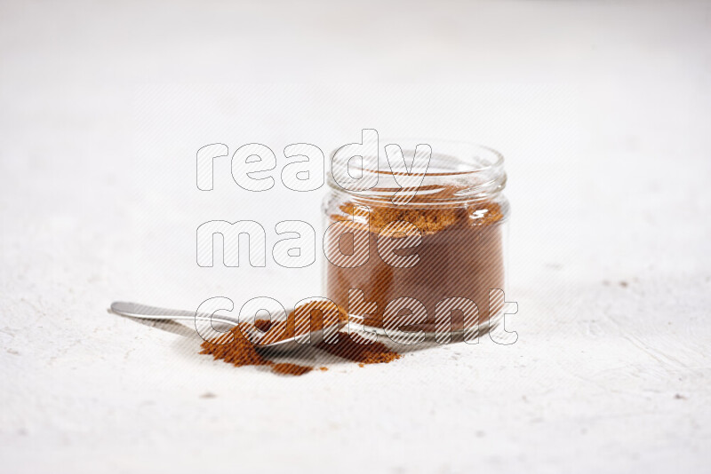 A glass jar full of ground paprika powder on white background