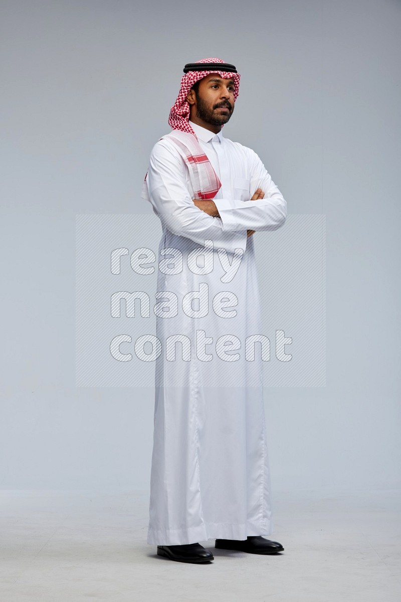 Saudi man Wearing Thob and shomag standing with crossed arms on Gray background