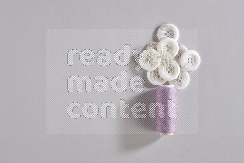 A purple sewing thread spool with small bunch of buttons on grey background