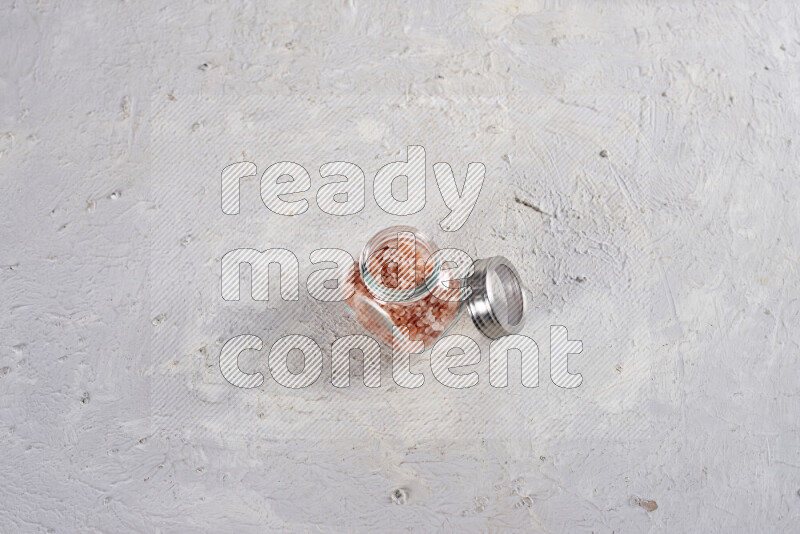 A glass jar full of coarse himalayan salt crystals on white background