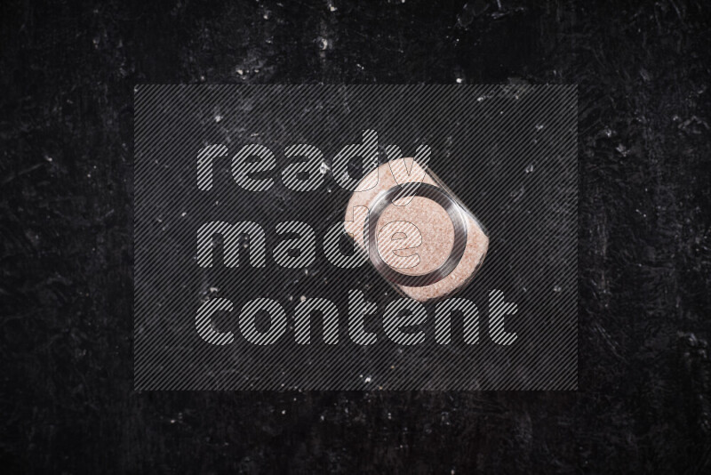 A glass jar full of fine himalayan salt on black background