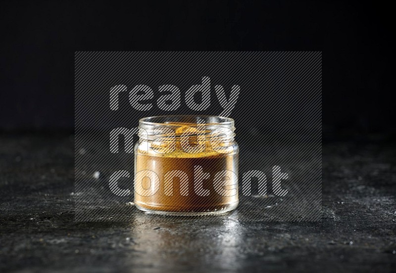 A glass jar full of turmeric powder on a textured black flooring